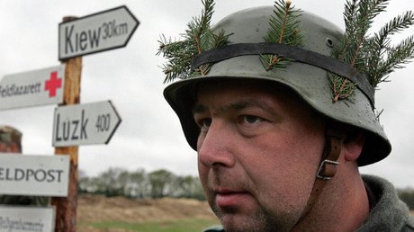 Un alemán con bigote de Hitler y casco nazi ataca a varios refugiados