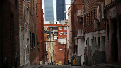 A man searches for food in a garbage container along a street, against the backdrop of the Four Towers business district pictured, in Tetuan