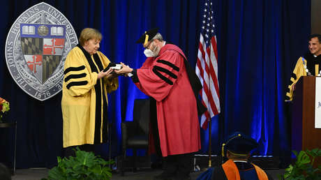 VIDEO: La interminable lucha de Angela Merkel para colocarse una toga durante una ceremonia en su honor